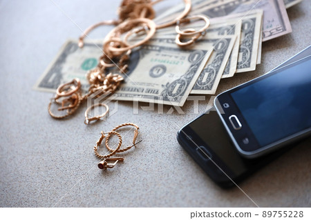 Many expensive golden jewerly rings, earrings and necklaces with big amount of US dollar bills close to smartphones. Pawn shop Many expensive golden jewerly rings, earrings and necklaces with big amount of US dollar bills close to smartphones. Pawn shop 89755228