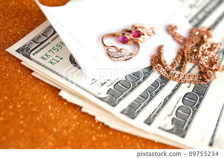 Expensive golden jewerly ring, earrings and necklace with big amount of US dollar bills on luxury glitter golden background surface. Pawnshop or jewerly shop 89755234