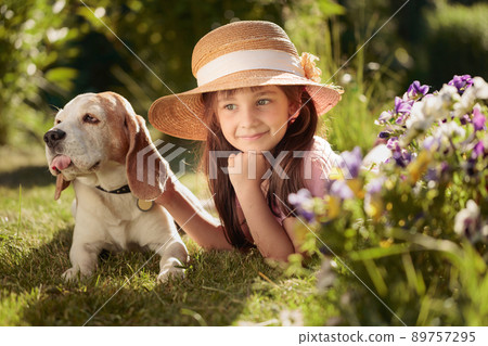 Happy little girl in a straw hat playing with his pet on the grass in the garden. Happy little girl in a straw hat playing with his pet on the grass in the garden. 89757295