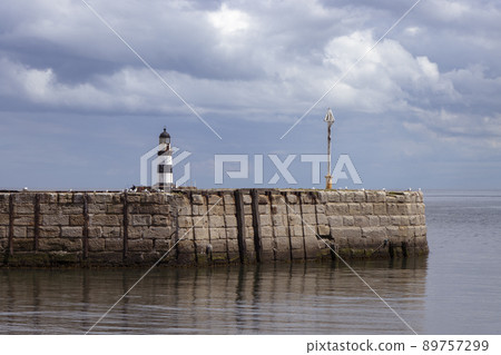 Iconic striped Seaham lighthouse on sea wall with cloud reflections Iconic striped Seaham lighthouse on sea wall with cloud reflections 89757299