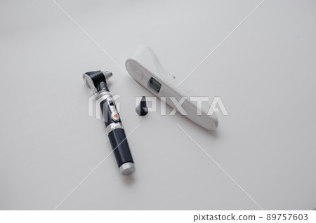 Non-contact thermometer on a white background for measuring body temperature. Otoscope on a white background, a device for examining the auricle and middle ear Non-contact thermometer on a white background for measuring body temperature. Otoscope on a white background, a device for examining the auricle and middle ear 89757603