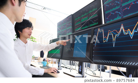 A business person who talks while pointing at the screen of multiple monitors 89757684