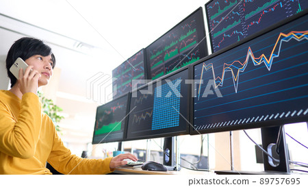 Image of a private investor trader talking on a smartphone while looking at the screen of multiple monitors Image of a private investor trader talking on a smartphone while looking at the screen of multiple monitors 89757695