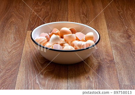 an iron bowl with eggshells stands on a wooden table top of a brown table, the remains of used chicken eggs are broken cracked shells. 89758013