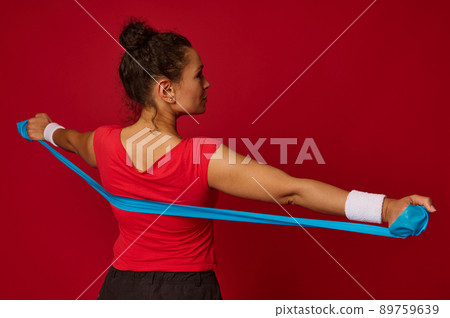 Close-up of beautiful Hispanic fit sportswoman working out with elastic rubber strap against red colored background with copy ad space Close-up of beautiful Hispanic fit sportswoman working out with elastic rubber strap against red colored background with copy ad space 89759639