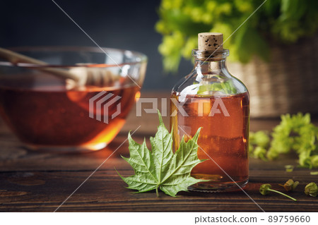 Bottle of maple syrup or healthy tincture and spring maple leaf. Bowl of maple syrup and wooden dipper on background. Bottle of maple syrup or healthy tincture and spring maple leaf. Bowl of maple syrup and wooden dipper on background. 89759660