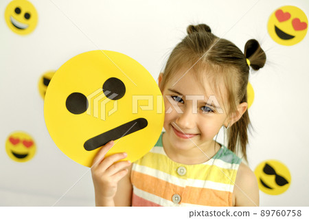 A cute beautiful smiling girl holds a cartoon cardboard sad face smile. A variety of emotions. Different Temperament A cute beautiful smiling girl holds a cartoon cardboard sad face smile. A variety of emotions. Different Temperament 89760758