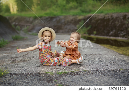 Ridiculous funny kids are sitting on rocks in a rocky area and laughing merrily. A girl takes a flower from her younger sister. Children play and indulge together. Summer holidays on vacation 89761120