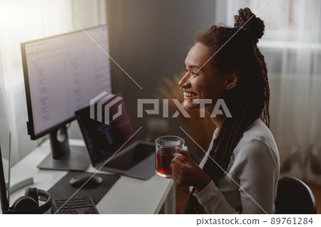 Close up portrait of joyful professional female programmer working on computer holding cup of tea Close up portrait of joyful professional female programmer working on computer holding cup of tea 89761284