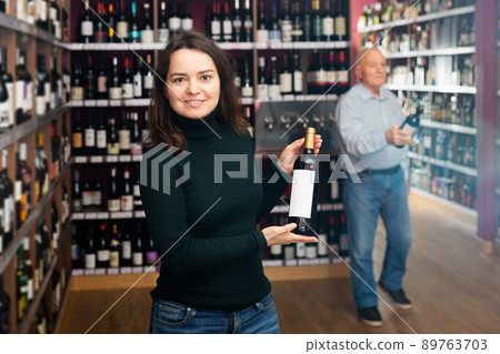 female customer selecting bottle of wine in shop female customer selecting bottle of wine in shop 89763703