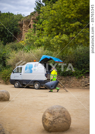 Barcelona, Spain - September 23, 2021: Cleaner on the parkway in Parc Guell. In the background the famous architecture. Famous tourist spot. Street cleaning in the park guell keep environment clean. Barcelona, Spain - September 23, 2021: Cleaner on the parkway in Parc Guell. In the background the famous architecture. Famous tourist spot. Street cleaning in the park guell keep environment clean. 89765345