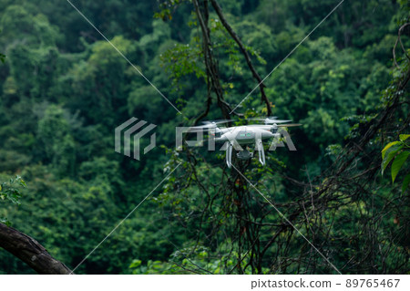 White drone with camera flying in summer forest White drone with camera flying in summer forest 89765467