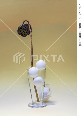 Still life with a dried lotus flower in a glass with white balls Still life with a dried lotus flower in a glass with white balls 89768207