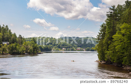On the the river Gatineau near Wakefield, Quebec, Canada. The riverbank invites you to swim in the cold water. Idyllic place for relaxing on off days. Shore surrounded by dense forest. White clouds On the the river Gatineau near Wakefield, Quebec, Canada. The riverbank invites you to swim in the cold water. Idyllic place for relaxing on off days. Shore surrounded by dense forest. White clouds 89768240