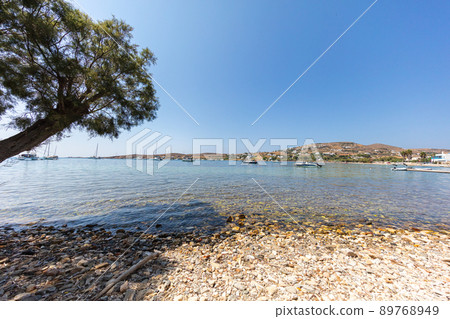 On the beach side of Paros. Livadia Beach, Paros island, Greece. The bay is near the ferry port. Rocky beach with crystal clear water. Panoramic view over the beach of Paros. Pine tree provides shade On the beach side of Paros. Livadia Beach, Paros island, Greece. The bay is near the ferry port. Rocky beach with crystal clear water. Panoramic view over the beach of Paros. Pine tree provides shade 89768949
