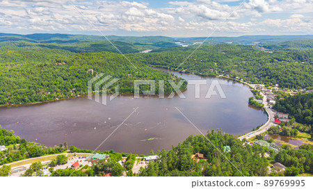 Aerial View of the Gatineau River near the village Wakefield, Canada. Clouds reflecting in the river water, a street with cars winds along the course of the river. Green lush Canadian forest landscape 89769995