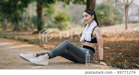 Athletic asian woman resting after a hard training in the mountains at sunset. Sport tight clothes 89771274