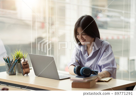 Online education. Asian girl with headphones makes an online lesson using a computer video call to a virtual teacher at home Online education. Asian girl with headphones makes an online lesson using a computer video call to a virtual teacher at home 89771291