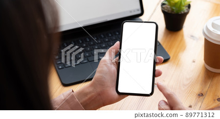 Top view Woman sitting on work desk and holding blank screen mock up mobile phone. 89771312