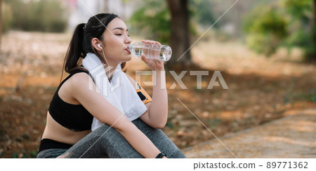 Young woman athlete takes a break, drinking water, out on a run on a hot day. Young woman athlete takes a break, drinking water, out on a run on a hot day. 89771362