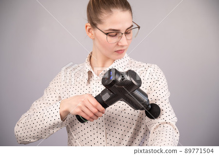 Caucasian business woman massaging her biceps with a percussion massager. Caucasian business woman massaging her biceps with a percussion massager. 89771504