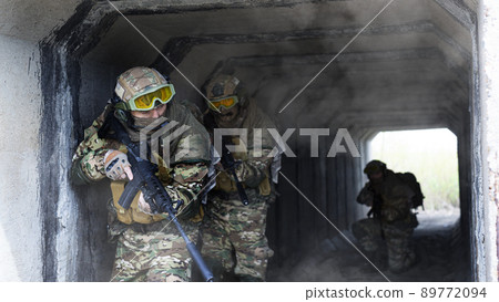 Three military mercenaries walk against a concrete wall background and smoke. Collage - one model in three poses. Photo format 16x9. 89772094