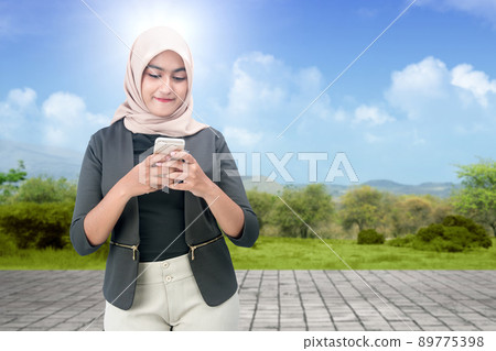Asian Muslim woman in a headscarf holding a mobile phone 89775398