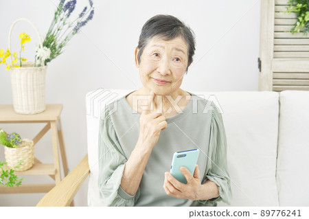 Female elderly smartphone thinking living room 89776241