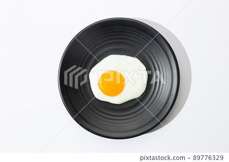 Fried egg on black plate on white background. 89776329