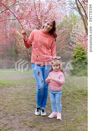 Happy mother and little daughter stand in park under pink cherry blossom . 89778394