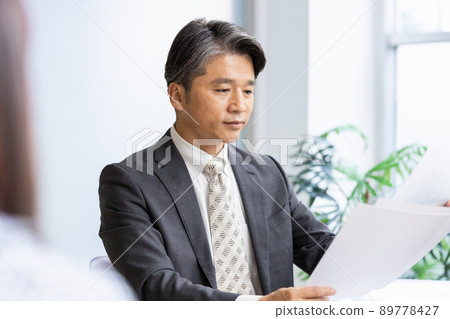 A businessman talking to the person in front while looking at the documents 89778427