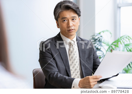A businessman talking to the person in front while looking at the documents 89778428