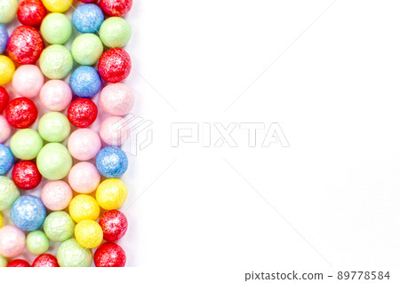Multi-colored round glossy balls of sugar confectionery topping lie at the left on a white background. 89778584