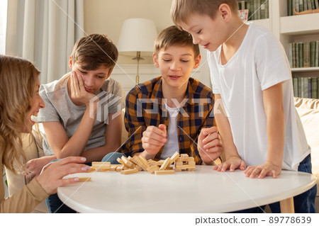 Three boys and a woman in the room are playing a board game made of wooden rectangular blocks 89778639
