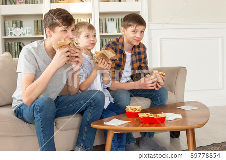 A cute three teenage boys, eating fast food in living room, watch tv A cute three teenage boys, eating fast food in living room, watch tv 89778854