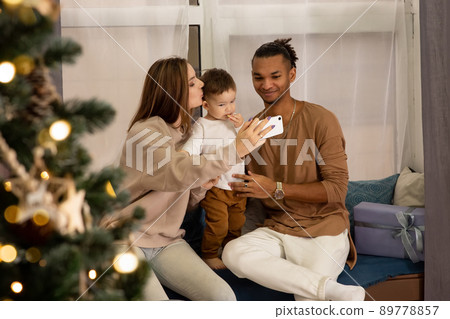 Happy family sitting at the window at home, taking a selfie on a smartphone Happy family sitting at the window at home, taking a selfie on a smartphone 89778857