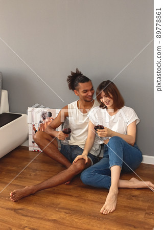 Happy stylish, modern, multiracial couple, a guy and a girl , sit at home on the floor against a gray wall 89778861