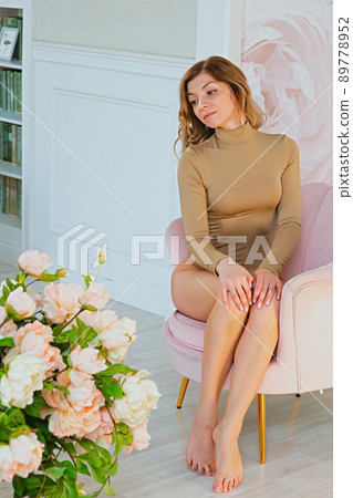 Portrait of a beautiful woman with blond hair, sits in a pink armchair, in the interior of the room Portrait of a beautiful woman with blond hair, sits in a pink armchair, in the interior of the room 89778952