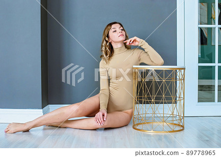 a beautiful woman with blond hair, in a beige long-sleeved swimsuit sits on floor a beautiful woman with blond hair, in a beige long-sleeved swimsuit sits on floor 89778965