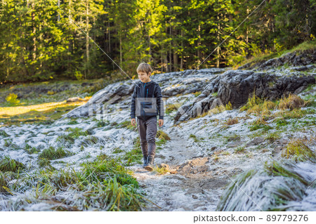 The boy is surprised at the first snow that fell on the green grass 89779276