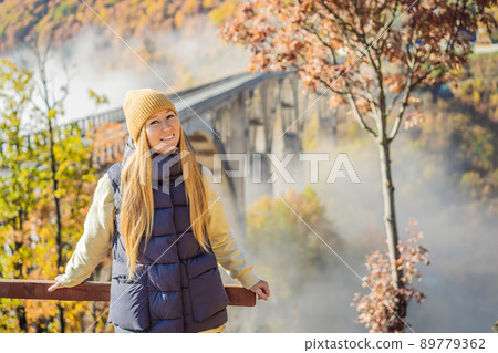 Montenegro. Woman touriste in background of Dzhurdzhevich Bridge Over The River Tara foggy morning. Travel around Montenegro concept. Sights of Montenegro 89779362