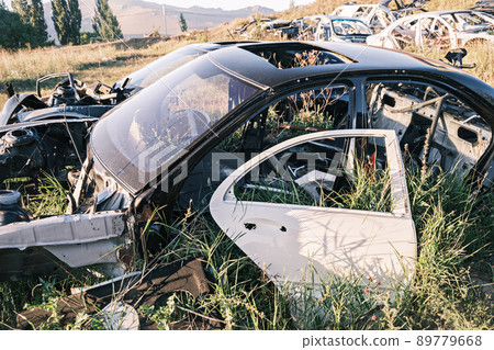 Car dump, scrap metal. Close-up of an old abandoned cars in a junkyard with grass sprouting inside and overgrown cobwebs. The sun reflects off the metal. Car dump, scrap metal. Close-up of an old abandoned cars in a junkyard with grass sprouting inside and overgrown cobwebs. The sun reflects off the metal. 89779668