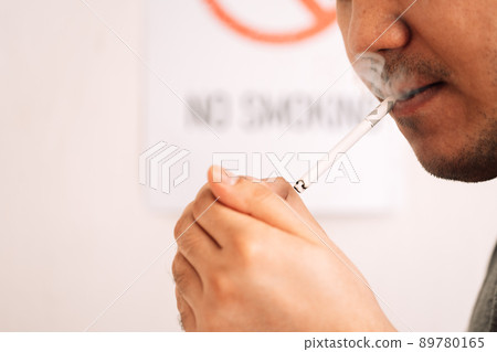 Man lights cigarette in front of sign no smoking Man lights cigarette in front of sign no smoking 89780165