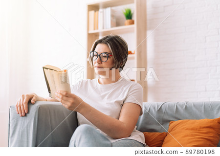 Girl with glasses reading book on the couch Girl with glasses reading book on the couch 89780198