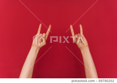 Female hands show rock and roll symbol against red background 89780202