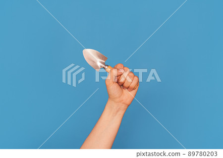 Woman's hand with small shovel against blue background 89780203
