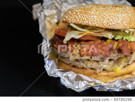 Closeup of big beef hamburger in food wrapping foil  .. Closeup of big beef hamburger in food wrapping foil  .. 89780298