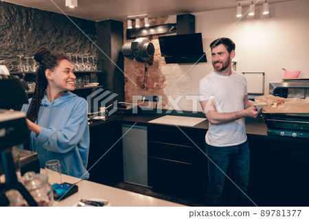 Cheerful young man and woman, co-workers smiling and preparing order in cafe. Bakery and coffee. 89781377