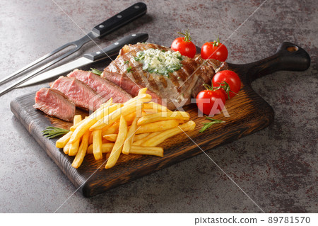 Grilled Ribeye Steak with French Fries, green butter and tomatoes closeup on the wooden board. Horizontal 89781570