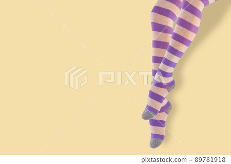 female legs hanging down, in pantyhose with lilac stripes, on a yellow background, concept 89781918